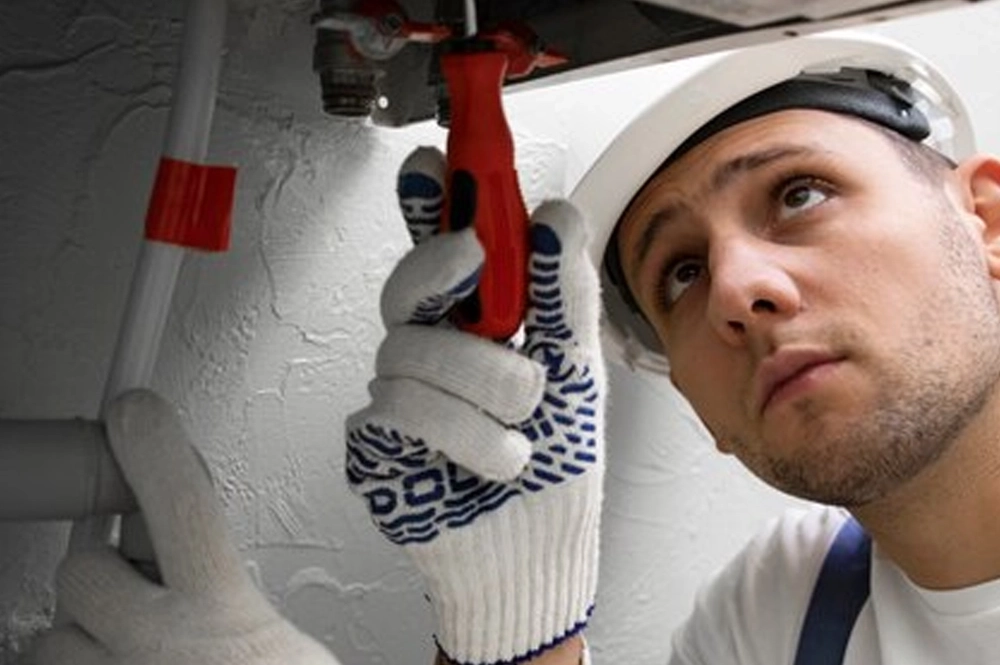 A technician in a white hard hat using a wrench to adjust a heating system pipe, demonstrating expert HVAC services for maintaining and repairing heating systems.