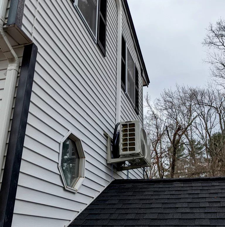 An outdoor mini-split air conditioning unit mounted on the side of a white house.