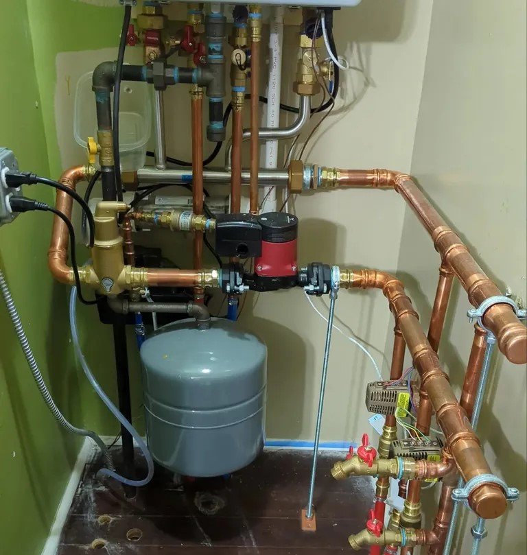 A compact indoor water heater and piping system with copper pipes and a pressure tank, installed in a utility space.